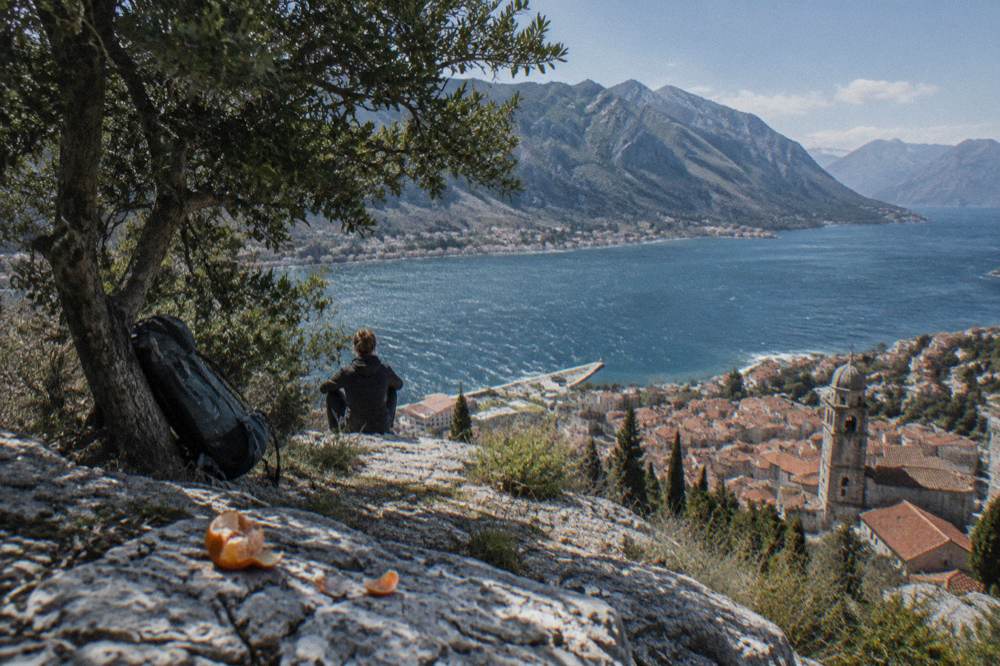 Hiker resting on a stone trail high above the blue Bay of Kotor