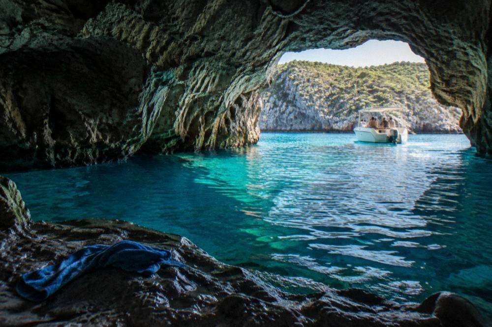 Turquoise water glowing inside a sea cave with a small boat waiting outside
