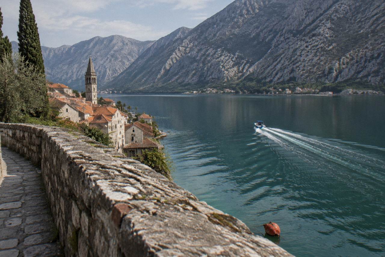 Blue speedboat crossing calm green water toward steep mountains on the Bay of Kotor