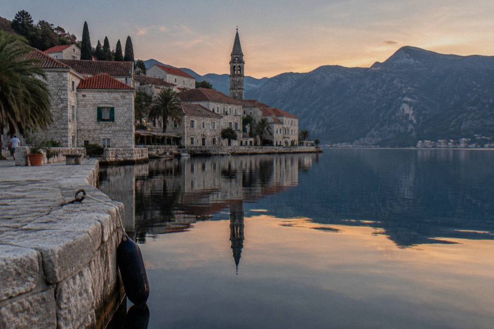Stone buildings of Perast reflected in still water along the Bay of Kotor waterfront