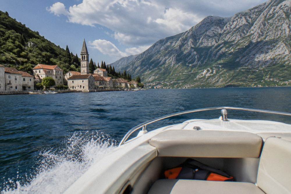 A speedboat crossing open water toward steep hillsides dropping into a bay.