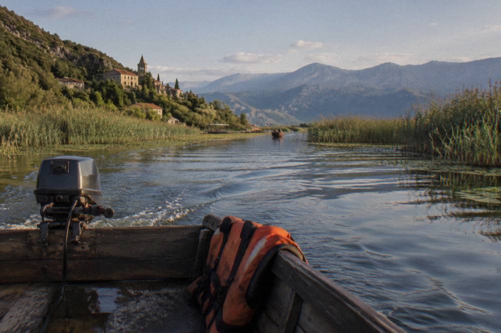 Traditional wooden boat on a wide lake with reed islands and distant mountains