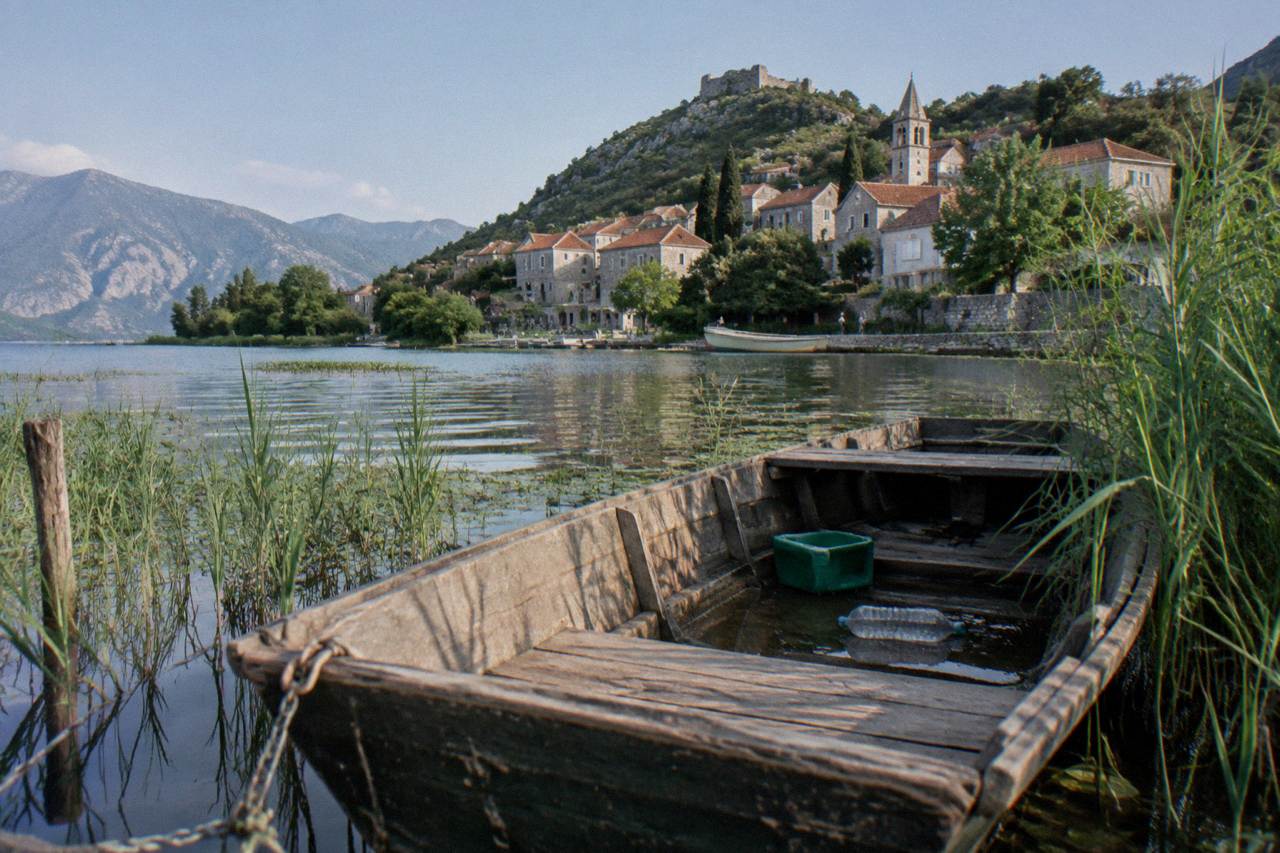 Wooden boat moored on calm lake water near reed beds and a hillside village