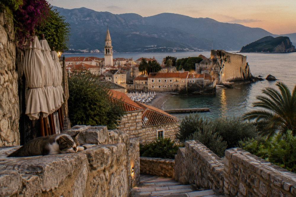 Stone buildings of a coastal town beside clear water with hillsides behind