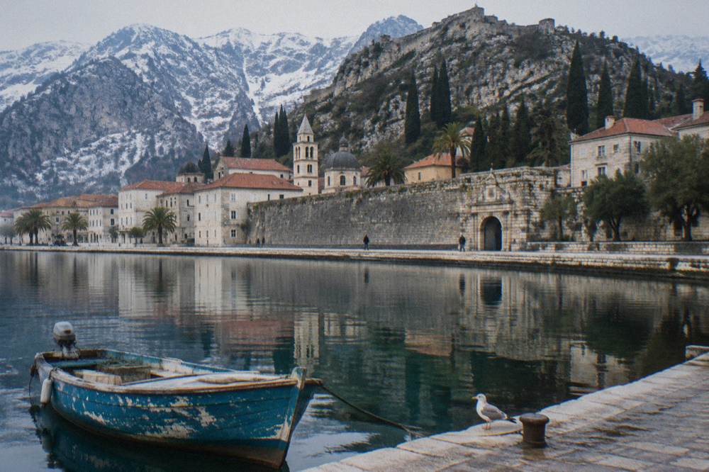 Walled old town beside a harbour with mountains reflected in still water