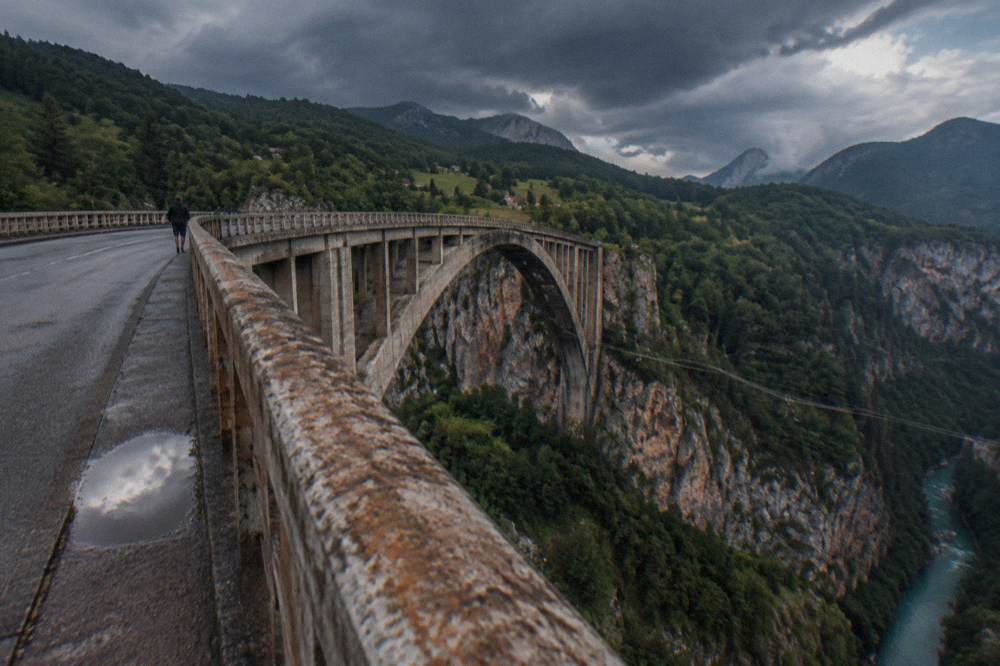 A tall arch bridge spanning a deep green river canyon with forested slopes on both sides