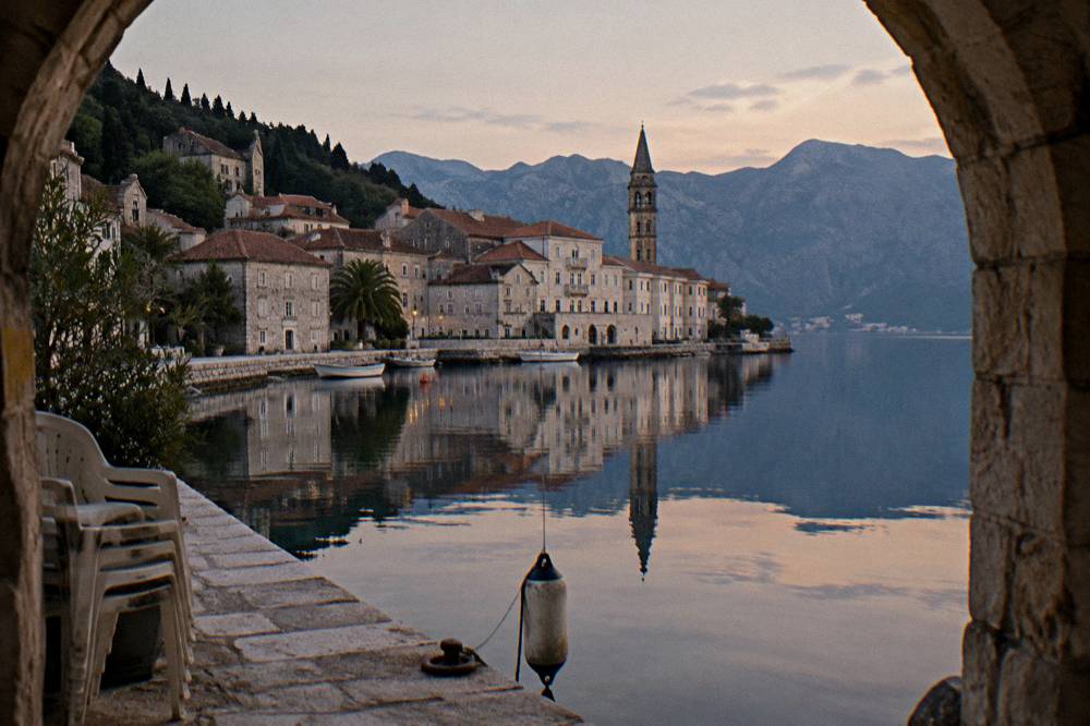 A small baroque stone town reflected in still water at the edge of a sheltered bay