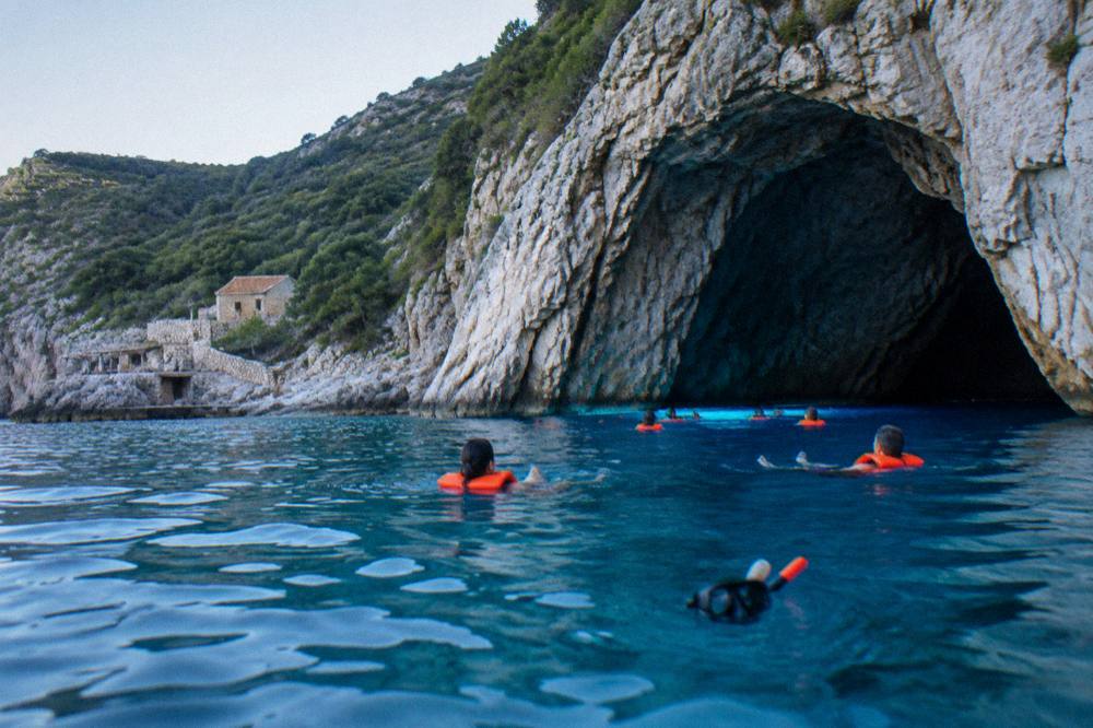 Swimmers in life jackets floating in bright blue water beside a rocky cave mouth