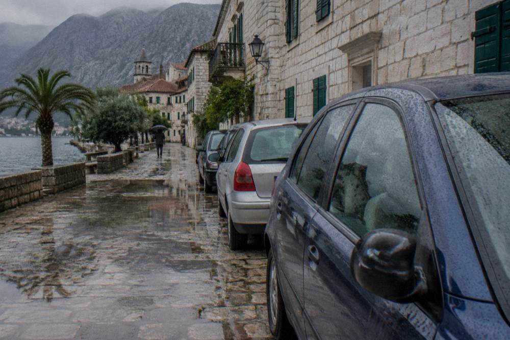 Parked cars on a stone street beside old stone buildings near Kotor old town