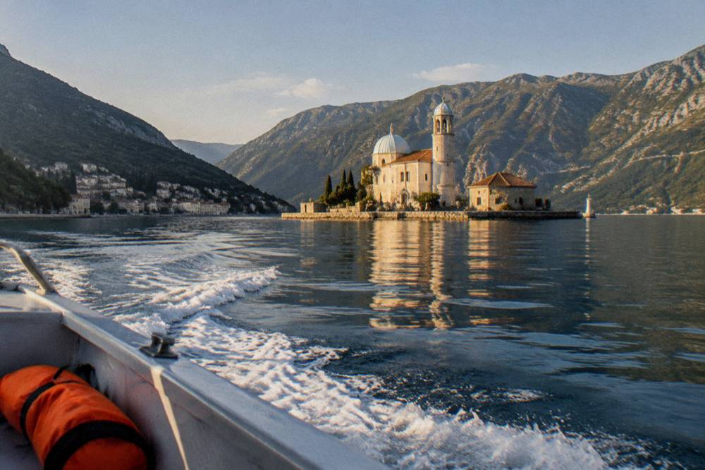 Speedboat crossing calm blue water toward a small island church in the bay
