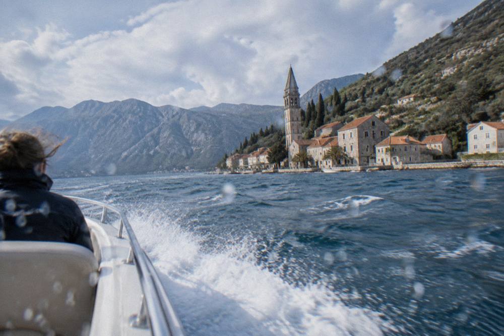 A speedboat cutting across the blue water of Bay of Kotor toward steep hills