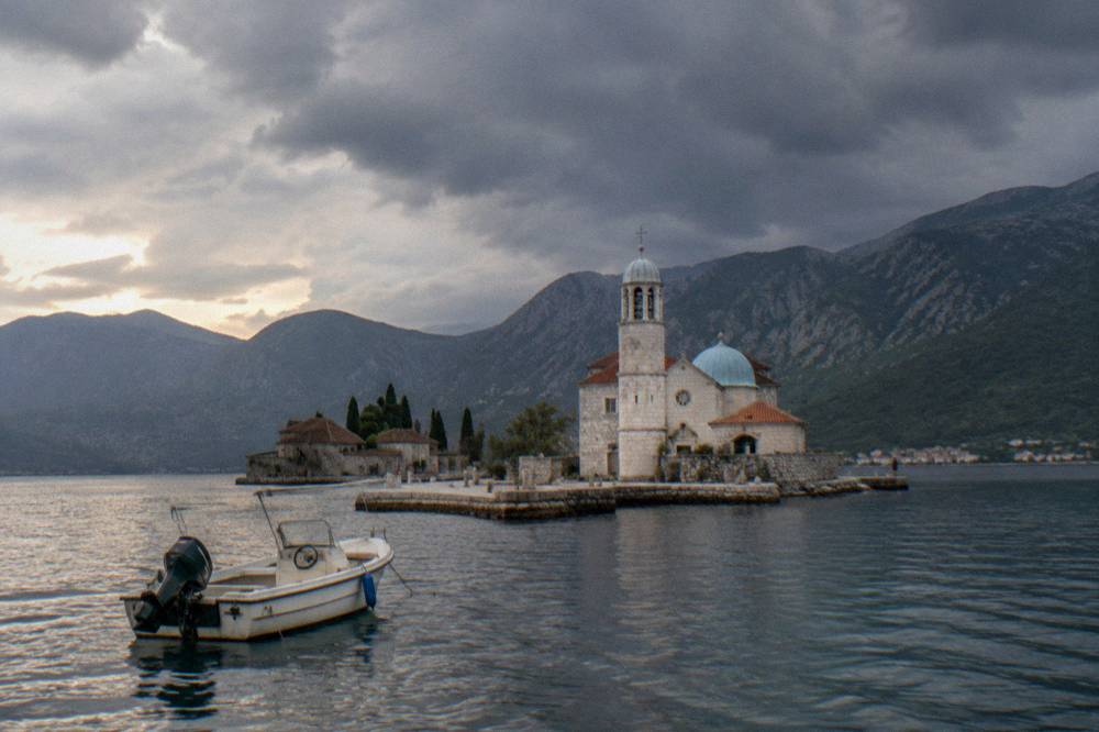 A small private motorboat anchored near a stone islet with a church tower