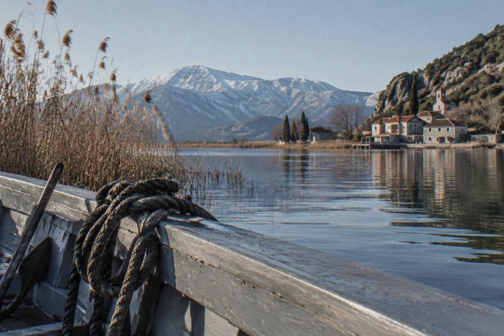 A wooden boat on a wide lake surrounded by reeds and distant mountains