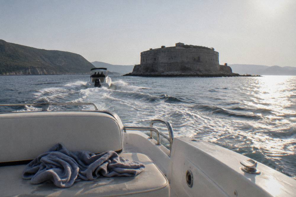 Two speedboats crossing open water toward a rocky coastline with a small island ahead