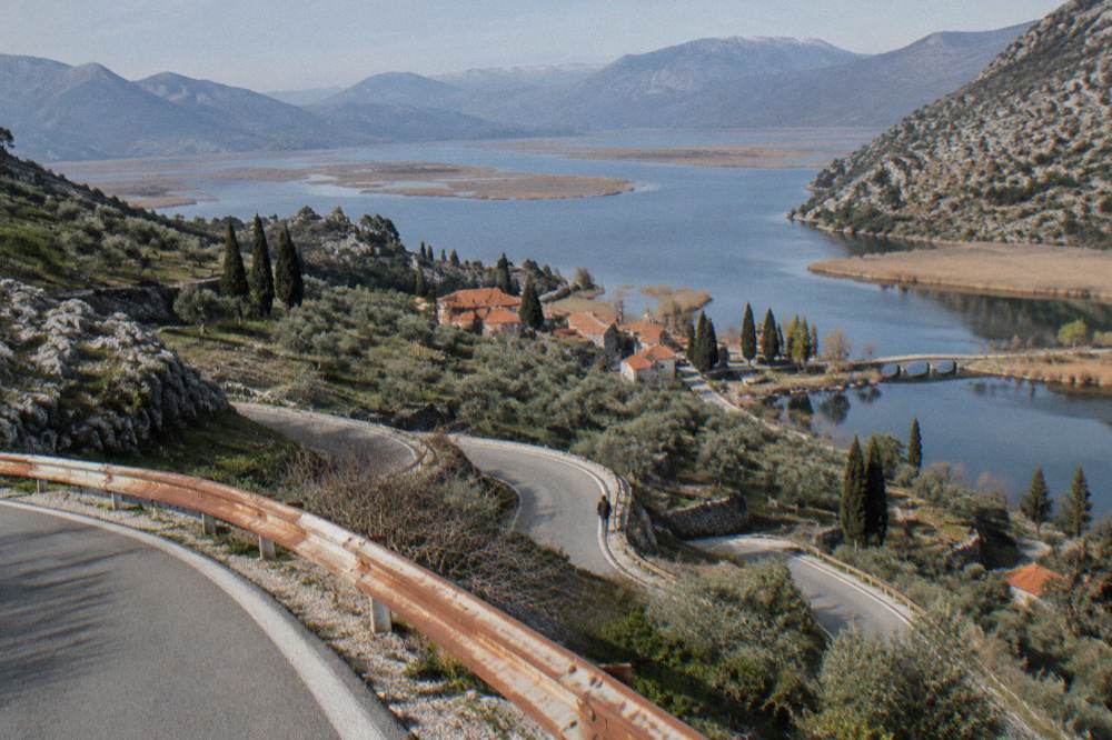 Winding road above a lake with reed islands and a distant stone bridge