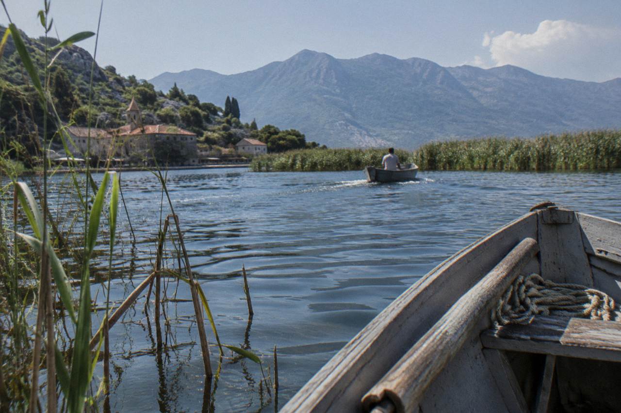 Wooden boat on a wide lake with reed beds and distant mountains under a clear sky