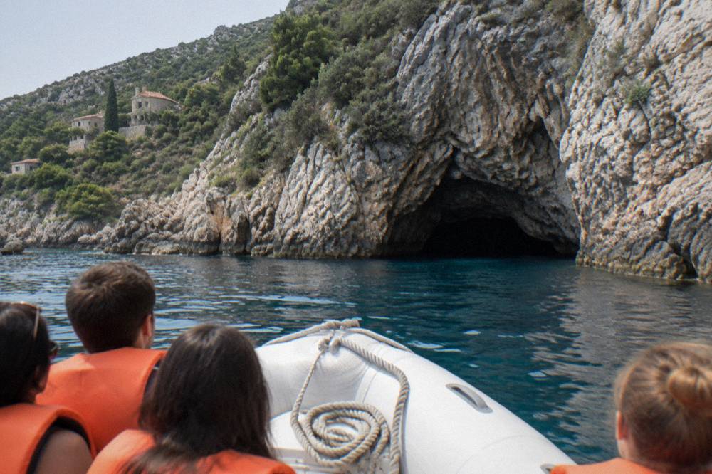Speedboat anchored outside a sea cave with passengers in life jackets preparing to swim