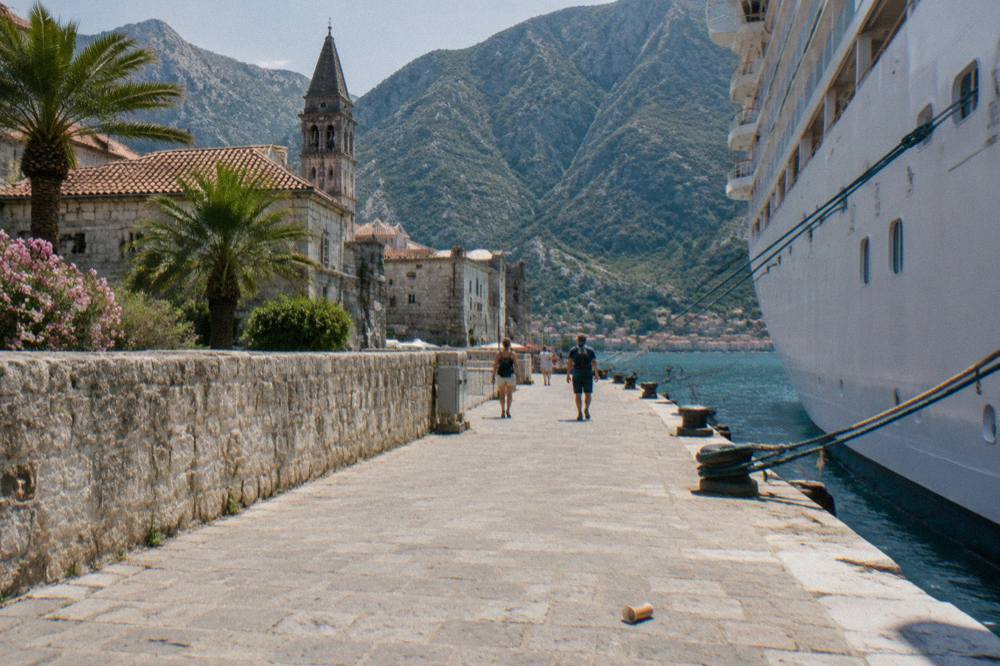 Cruise ship docked at the Kotor waterfront with the old town walls and mountains behind it