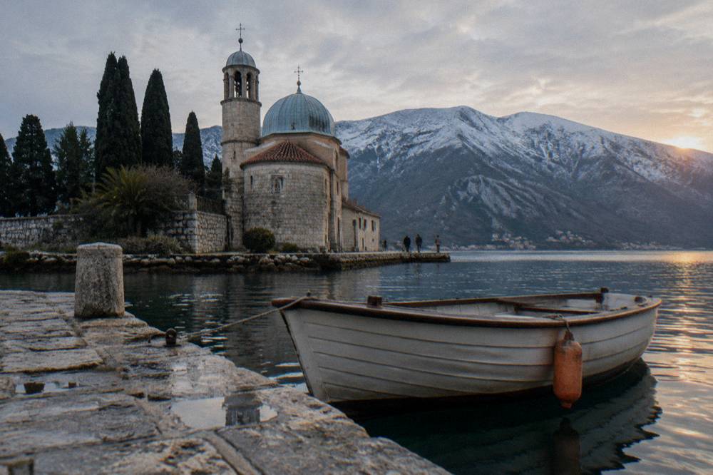 Small wooden boat near an island church in the Bay of Kotor with mountains across the water