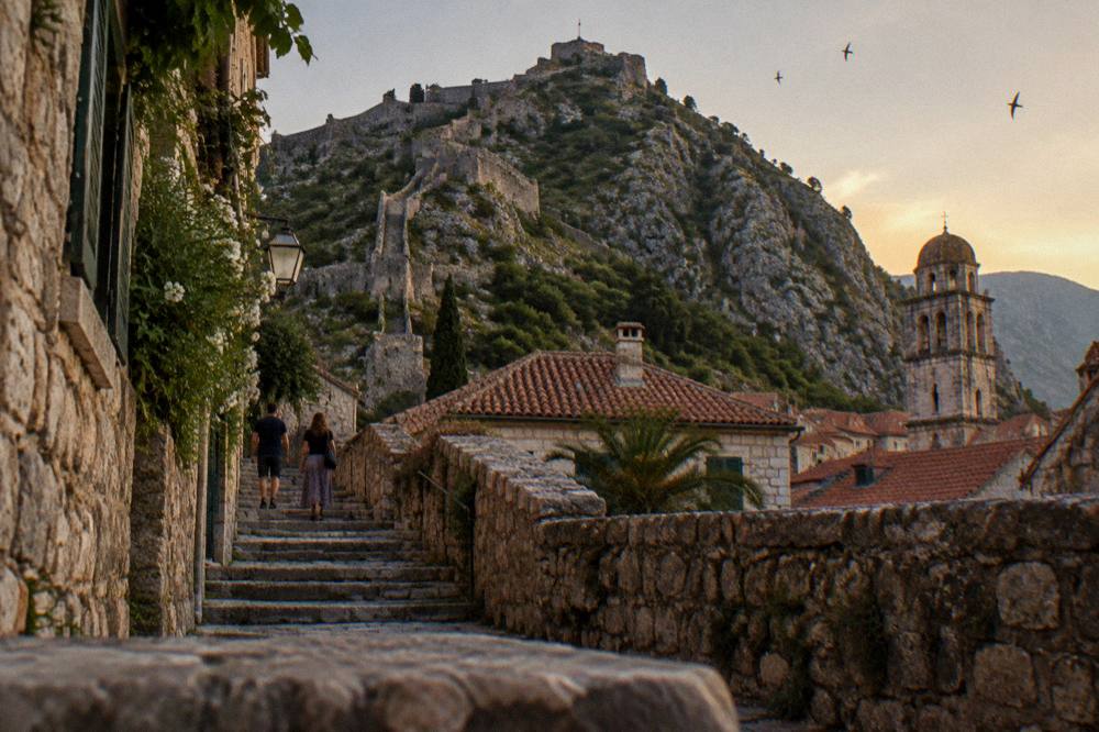 Stone ramparts of Kotor fortress rising above red roofs toward a mountain peak