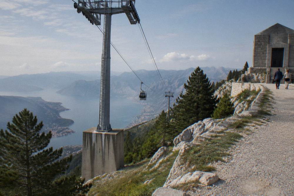 Cable car cables rising over pine slopes toward a mountain ridge above Kotor