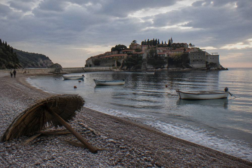 Stone houses and a church tower along a narrow bay shoreline with boats moored nearby