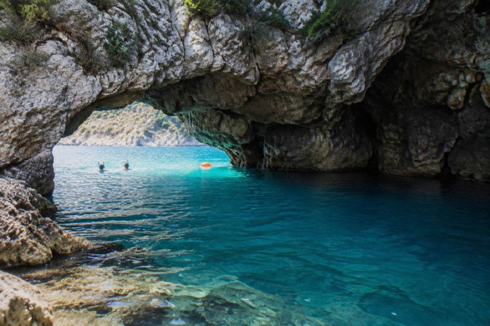 Clear turquoise water at the mouth of a sea cave with a rocky cliff above