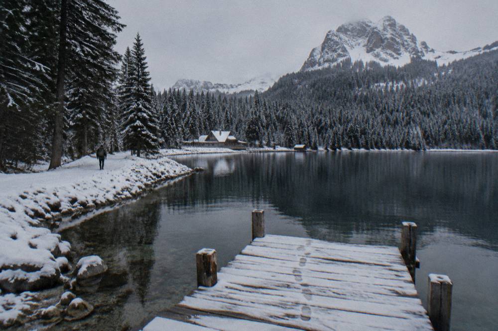 A mountain lake ringed by pine forest with a wooden jetty in the foreground