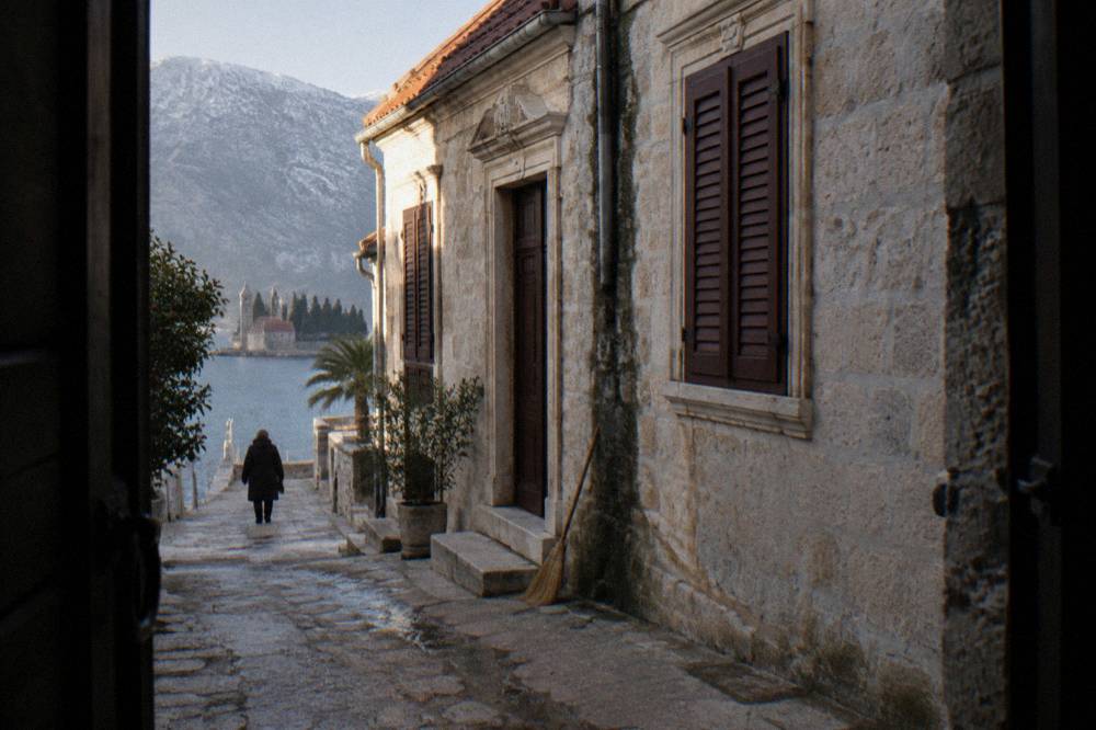Narrow stone lane in Perast with baroque church facades and closed shutters