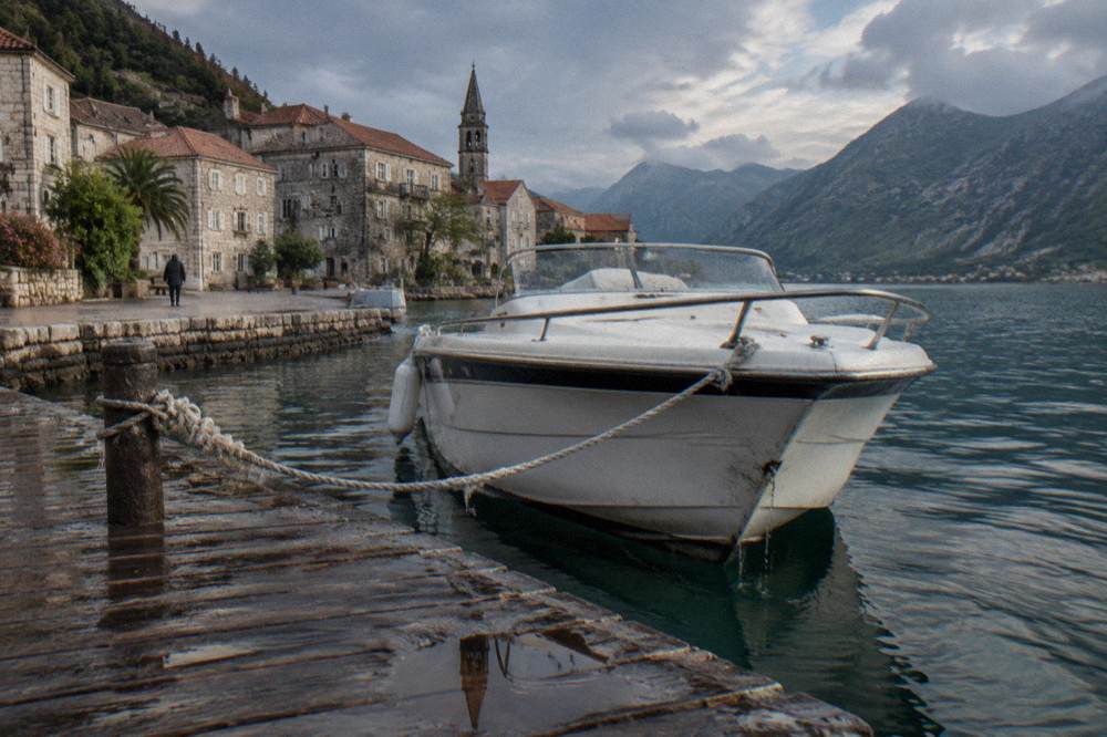 White speedboat moored at a wooden jetty with Perast waterfront buildings behind