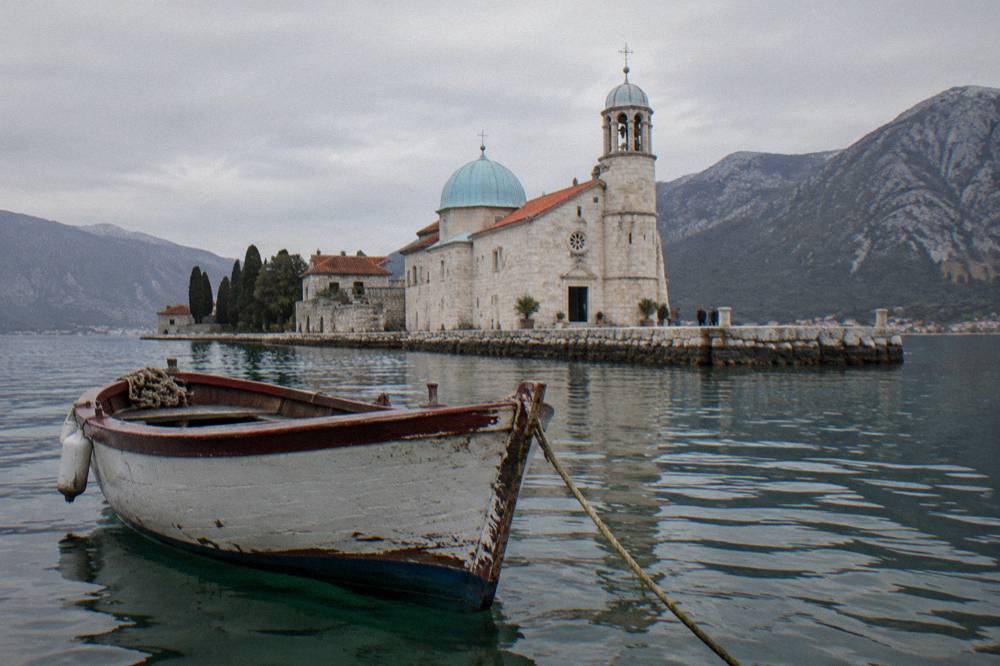 Small boat anchored near a stone island chapel with calm green water and low hills behind