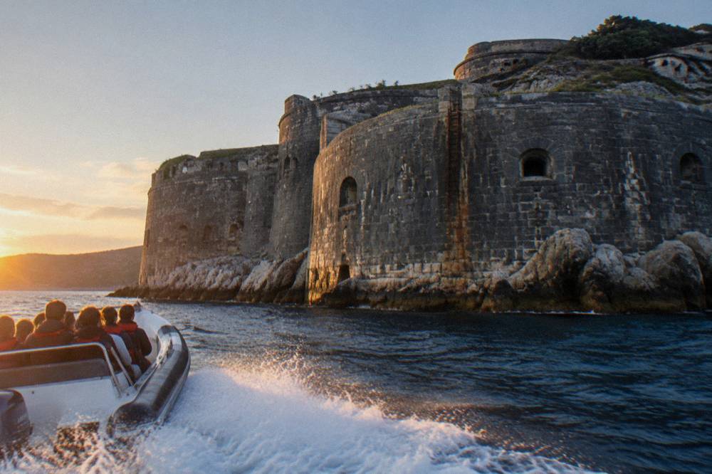 A speedboat with passengers circling Mamula Island fortress close to the stone walls