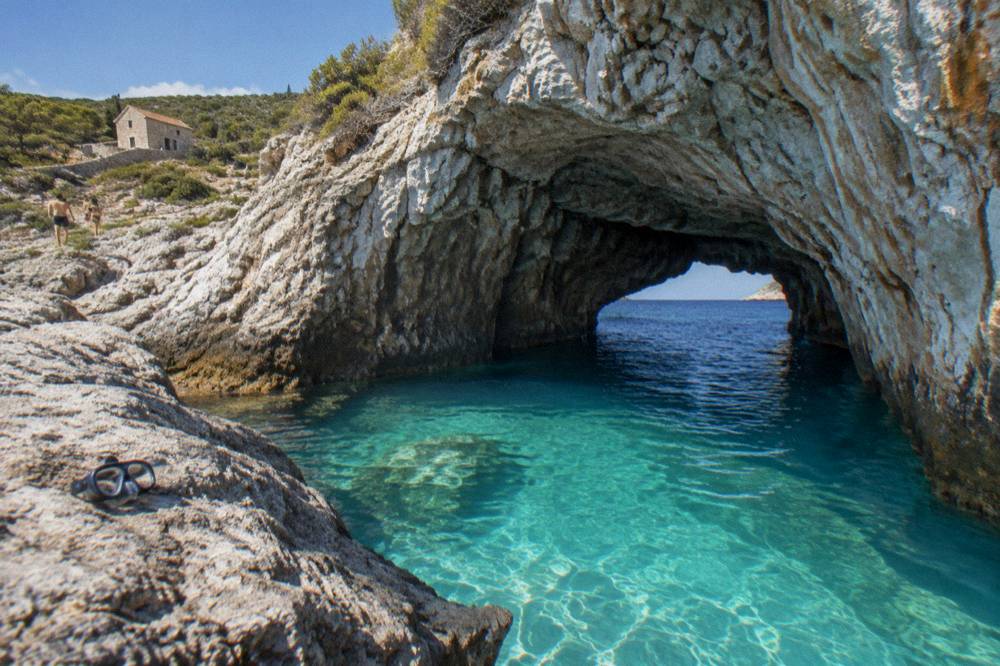 The Blue Cave entrance with turquoise water and a rocky coastline under a blue sky