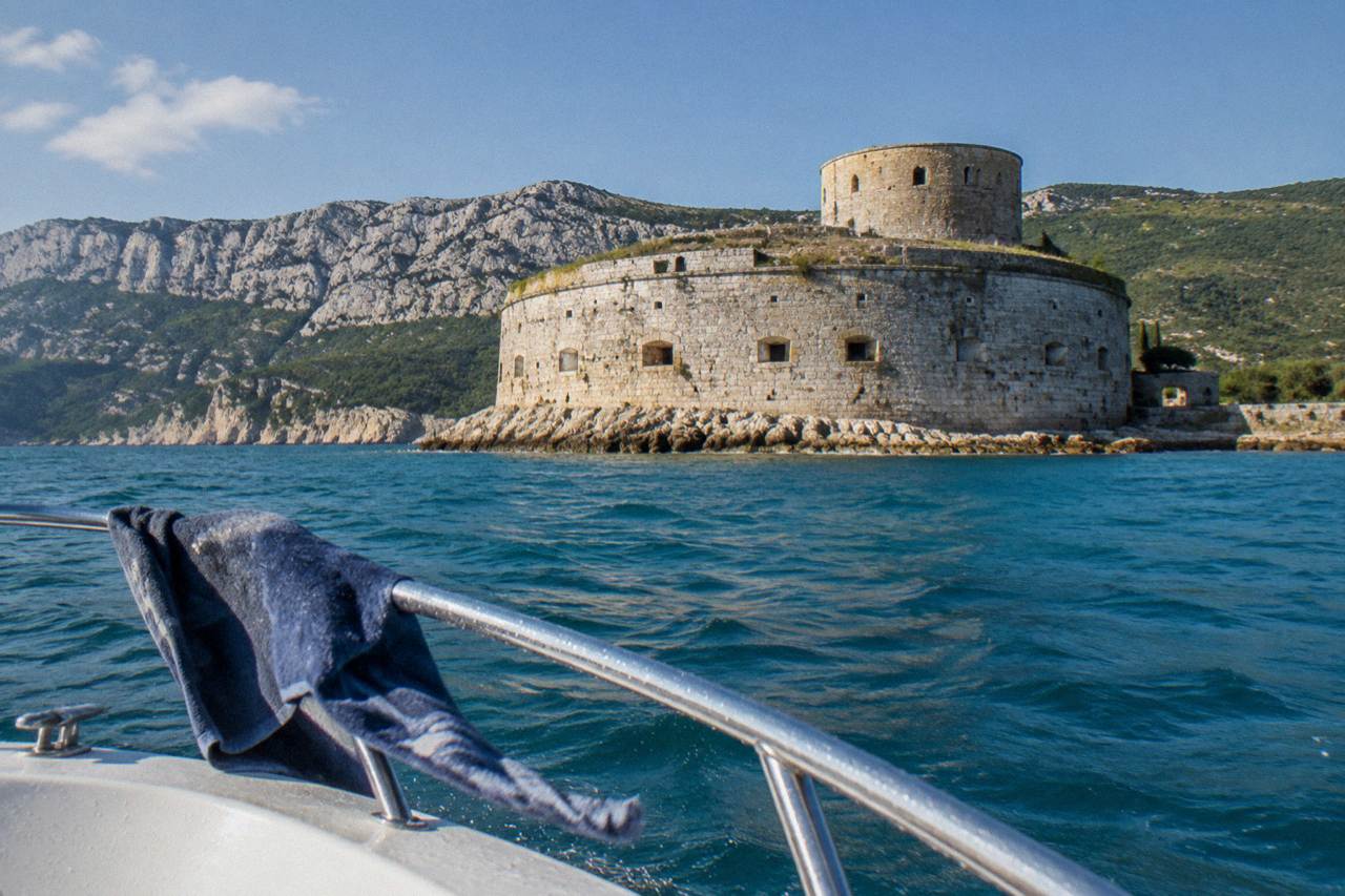 Mamula Island fortress seen from a speedboat on a sunny day with turquoise water and rocky coastline
