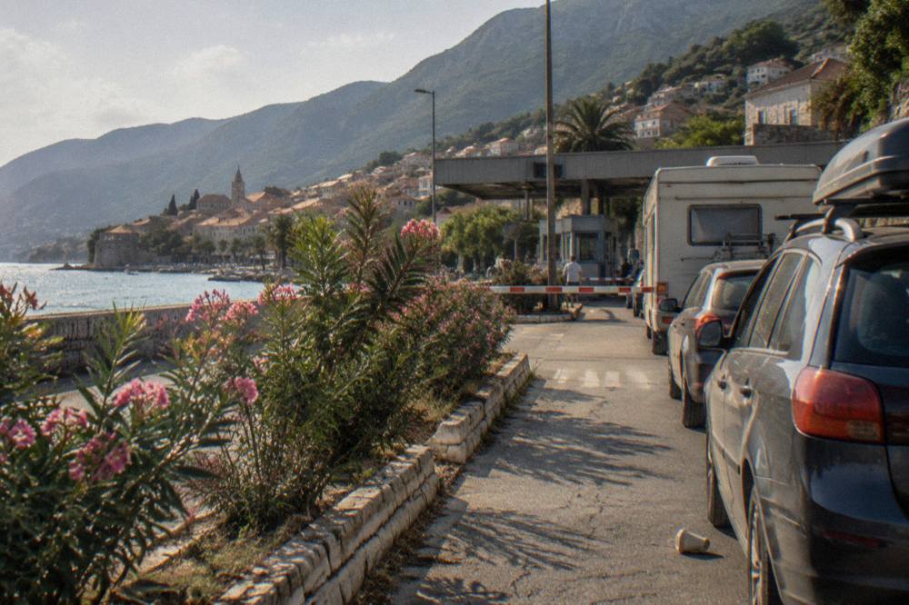 Rows of cars queuing at a border checkpoint booth on a summer afternoon