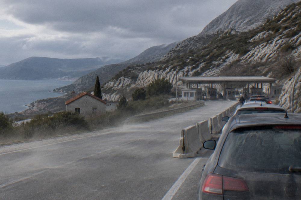 Cars waiting in a queue at a border checkpoint with hills behind
