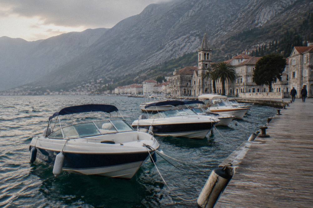 Speedboats moored at a wooden jetty on the Bay of Kotor beneath steep hillsides