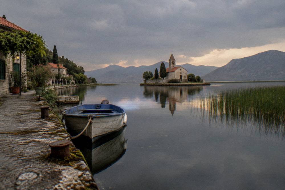 Fishing village church tower reflected in still lake water with hills fading into haze