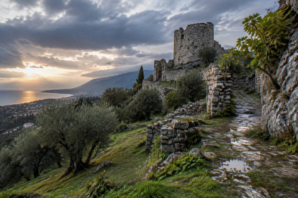 Ruined stone walls and a fortress tower of an abandoned hilltop old town above olive trees