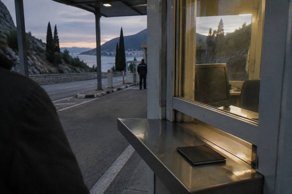 A passport held open at a small border control window with hills behind