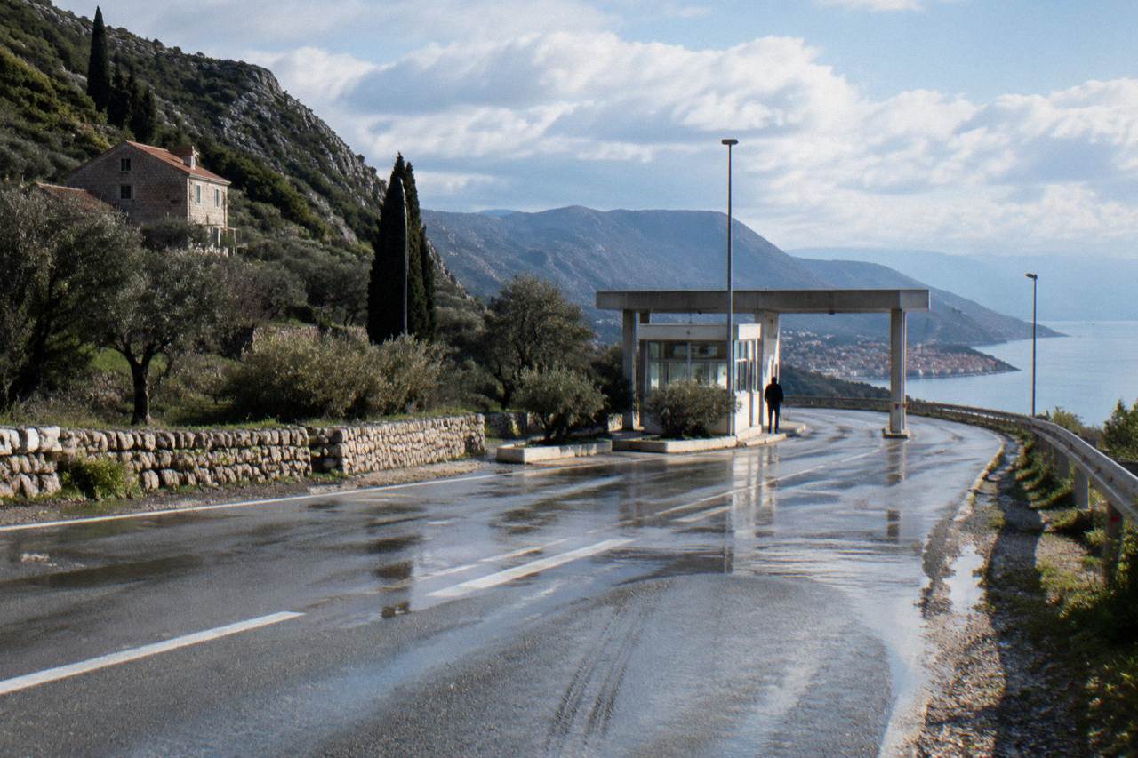A border checkpoint booth on a coastal road between hills and the sea
