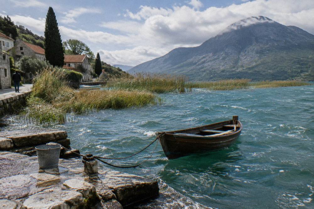 A small wooden boat on a wide lake with reed beds and distant mountains