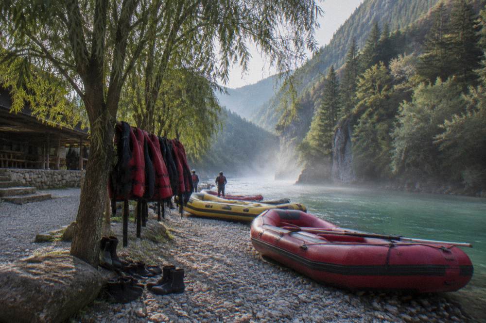 An emerald river running through a deep forested canyon with rafting boats at a gravel bank
