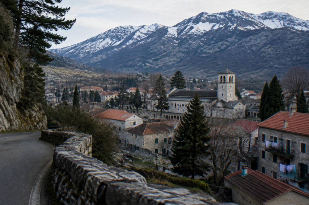 A stone mountain village with old grey houses and a church tower beneath high peaks