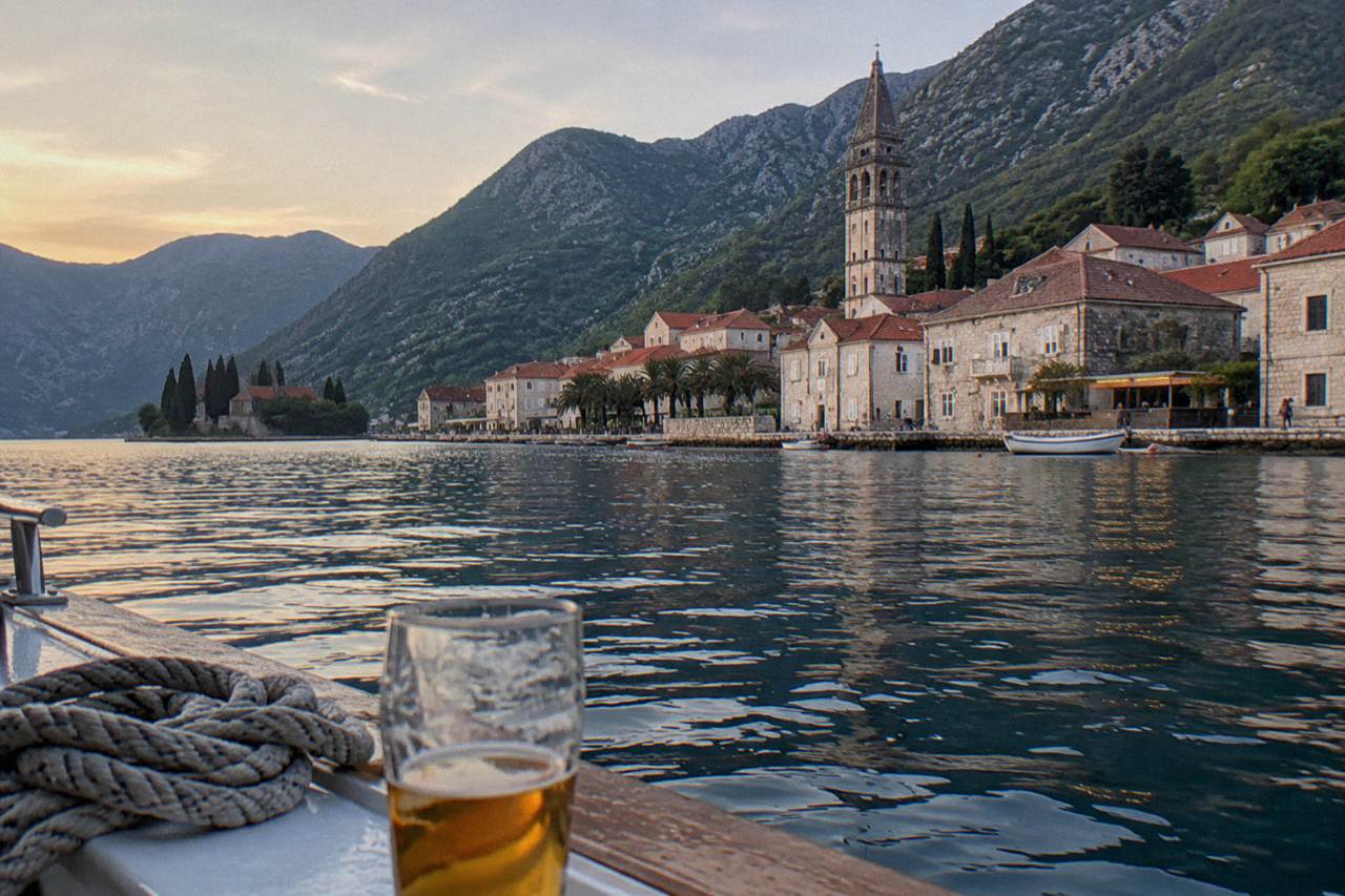 Red-roofed stone houses of Perast rising above the blue water of the Bay of Kotor with green mountains behind