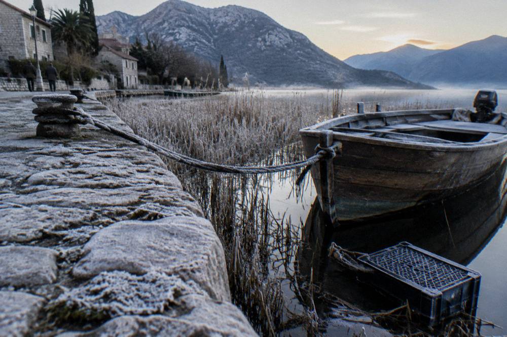 A wooden boat moored at a small stone quay on Lake Skadar near reed beds