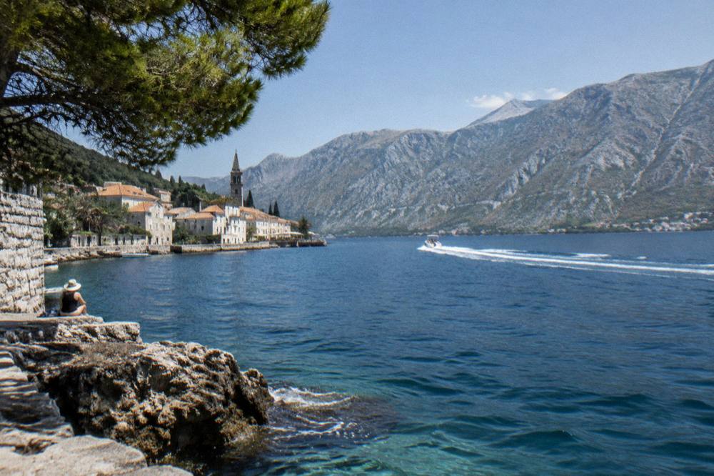 A speedboat cutting across the open blue water of the Bay of Kotor toward distant mountains