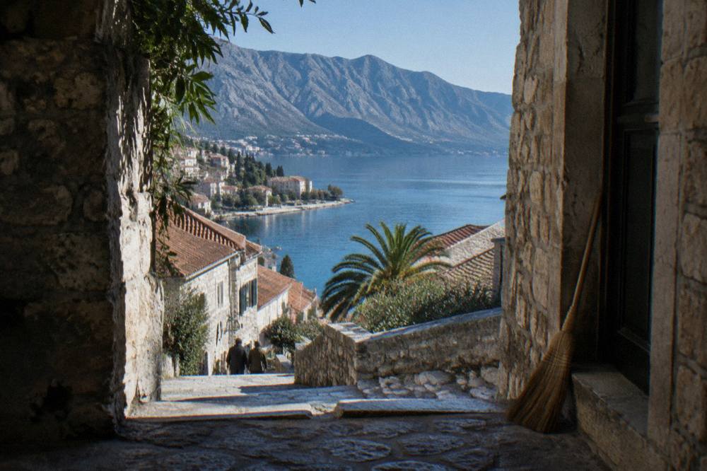 Steep mountains dropping straight into a calm blue bay with a small stone town at the shoreline