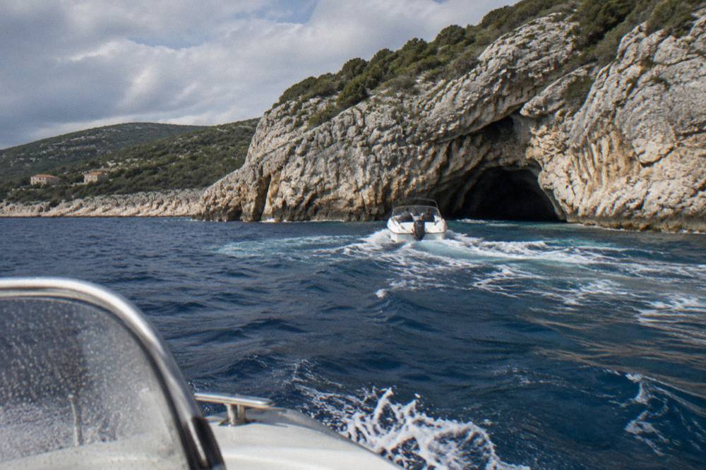 Speedboat crossing open blue water toward rocky cliffs with a cave entrance