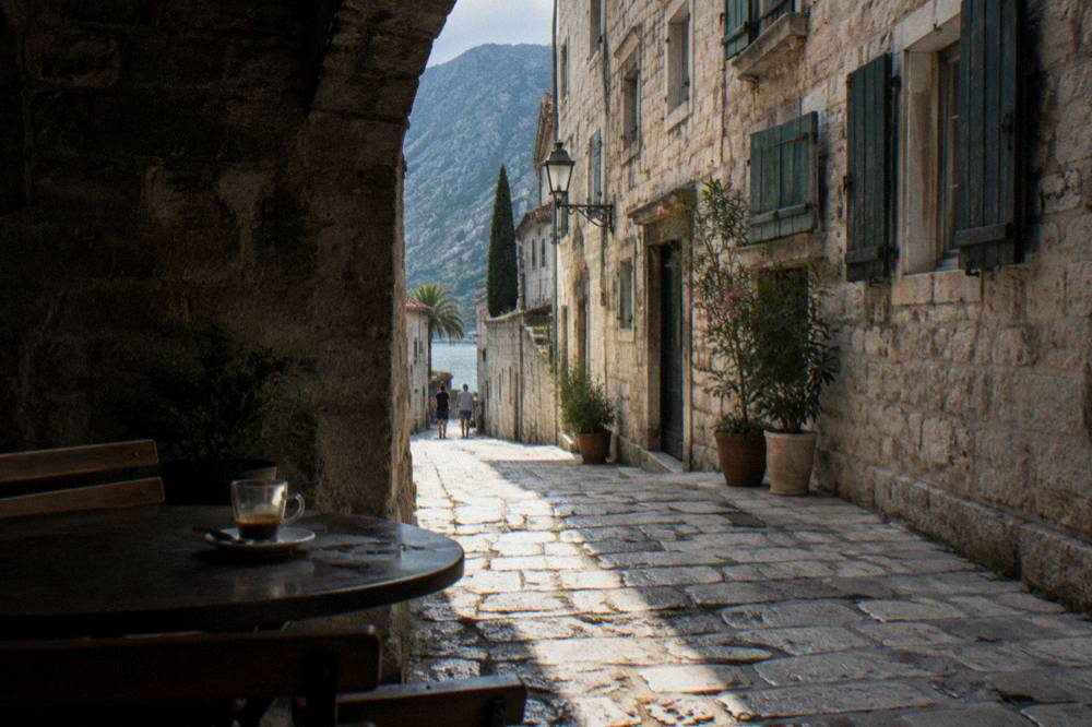 Narrow stone street in a walled medieval town with shuttered buildings and cafe tables